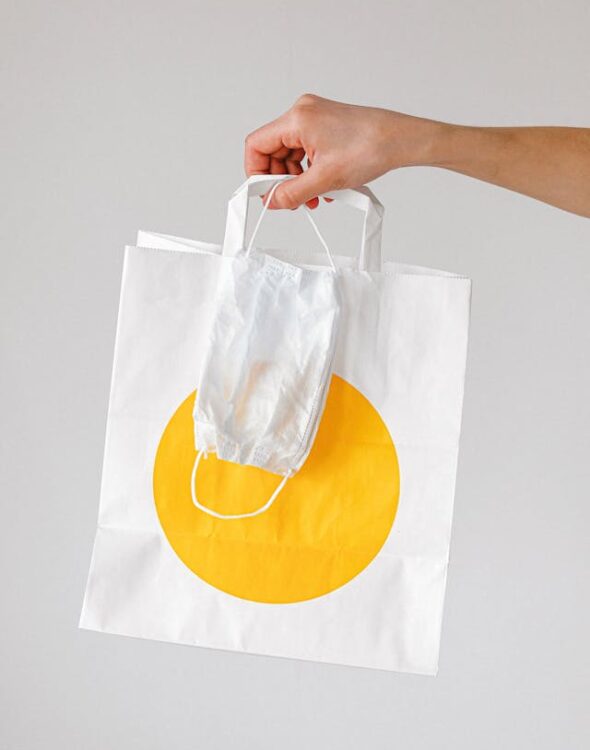Hand holding a paper grocery delivery bag with a face mask