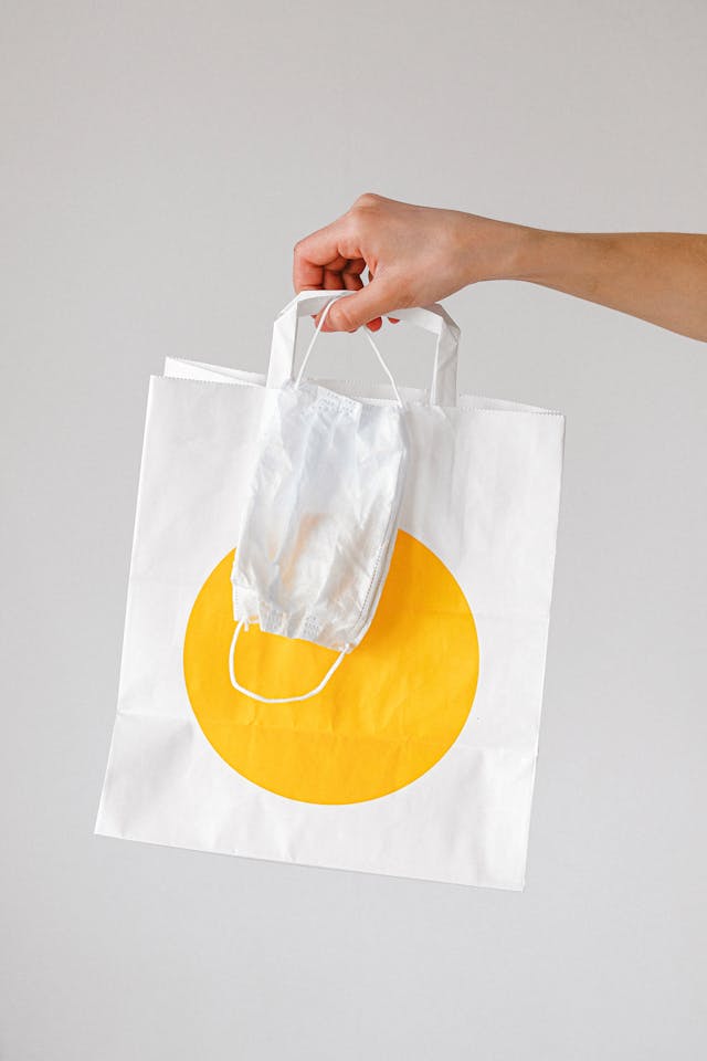 Hand holding a paper grocery delivery bag with a face mask