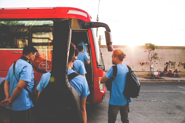 Group of tourists boarding a red charter bus at sunset